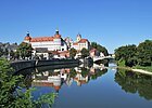 Schloss Neuburg und die Donau, die sich rechts am Schloss vorbeischlängelt. Links ist die Promenade und links das begrünte Ufer zu sehen.
