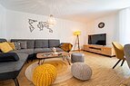 Wohnzimmer der Kirche Sankt Lukas mit Sofa, einem Fernsehen und einem gemütlichen Tisch mit Hocker.
