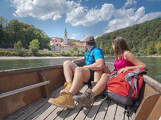 Zillenfahrt am Kloster Weltenburg In dem hölzernen Boot sitzen ein Mann und eine Frau, beide in Wanderkleidung mit dem Blick Richtung Kloster Weltenburg gerichtet. Das Kloster ist im Hintergrund von weitem zu sehen umrahmt von grünen Wäldern.