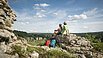 Ein Pärchen sitzt auf einem Felsen. Ihre Wanderrucksäcke lehnen daran. Sie lassen ihren Blick ins Tal schweifen.