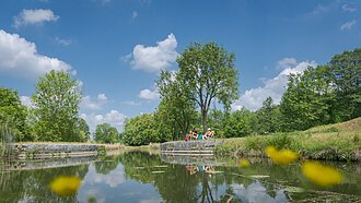 Ludwig-Donau-Main-Kanal bei Berching Am Ludwig-Donau-Main-Kanal der mittig fließt, haben es sich ein Pärchen am rechten Ufer in Liegestühlen gemütlich gemacht. Rechts und links stehen Bäume, der Himmel strahlt in blau.